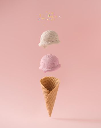 Ice cream scoops, colorful sprinkles, and waffle cone separated on pink background