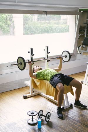 Man in green t-shirt lifting heavy bar exercising upper body