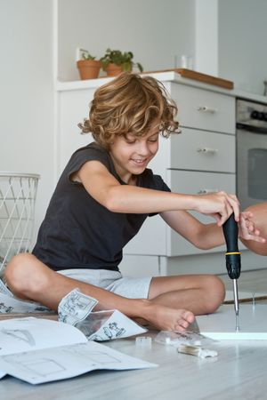 Cheerful boy using screwdriver during furniture assembly