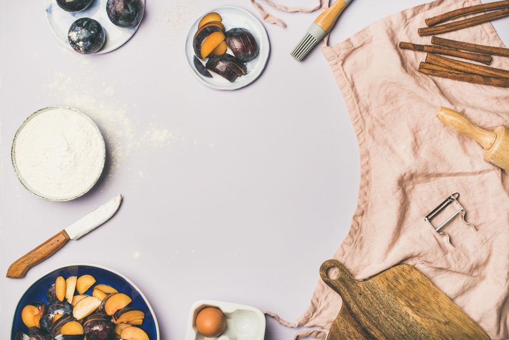 Baking ingredients and tools, plums, pastry brush, cinnamon, eggs on pastel background, copy space
