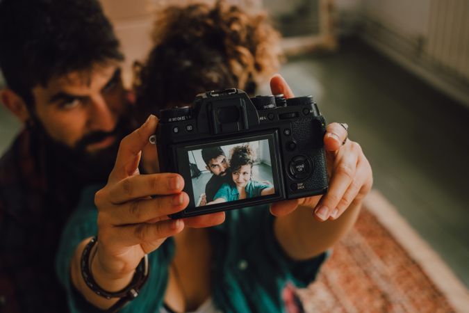 Joyful couple embracing and taking selfie on camera at home