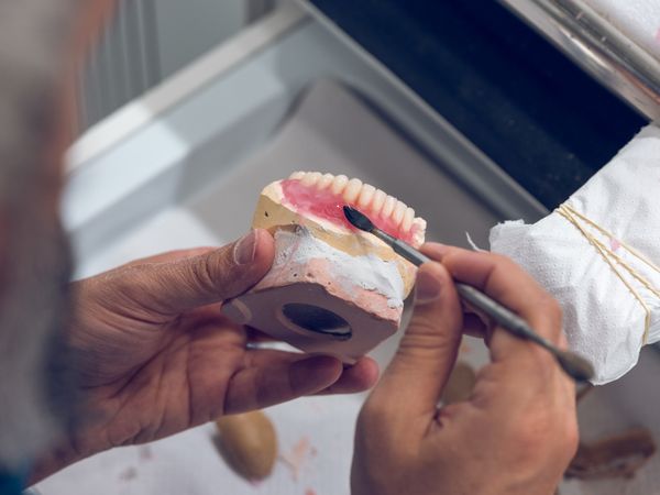 Crop dentist technician applying steel spatula on jaw implants