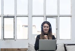 Woman in headphones sitting on sofa and using laptop