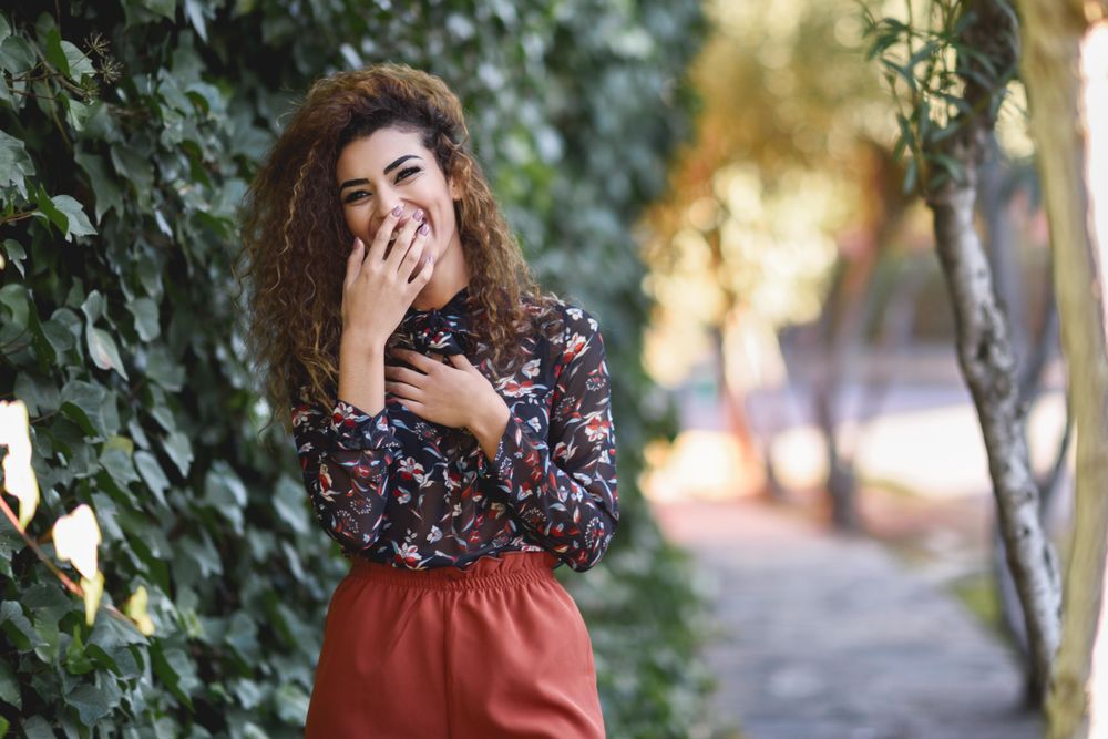 Smiling Arab woman wearing casual clothes in the street lined with greenery