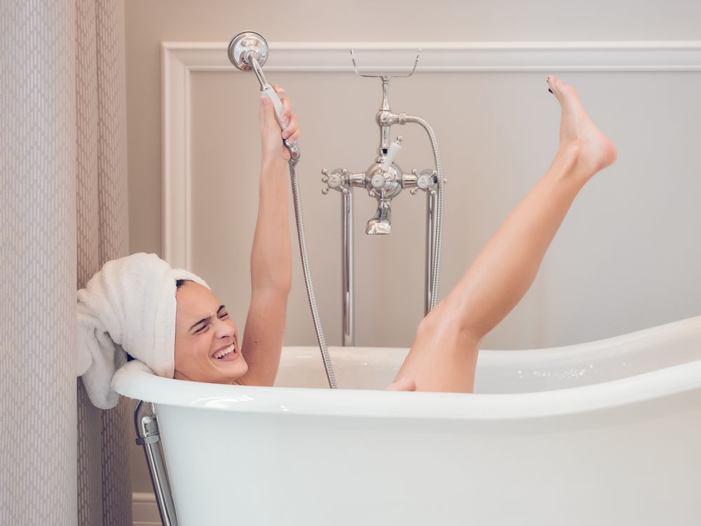 Cheerful woman lying in bathtub raising arm and leg
