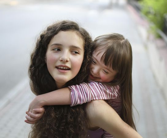 Portrait of little sister giving her big sister a hug while on a piggyback ride