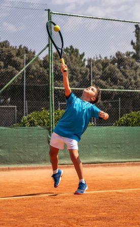Little boy playing tennis on a dirt court