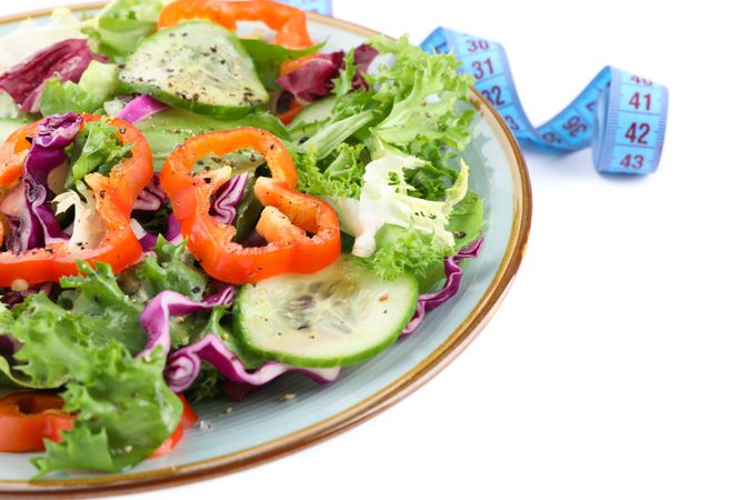 Plate with fresh salad and measuring tape isolated on plain background
