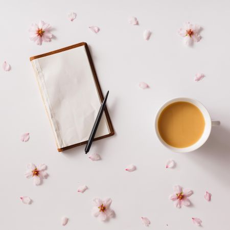 Vintage notebook on light background with pink flowers and cup of coffee