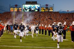 Football team running across field during evening game with marching band playing