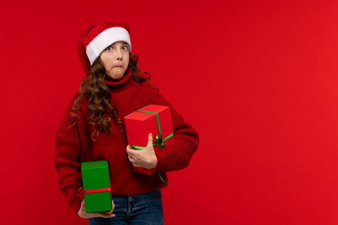 Surprised girl in Santa hat holds Christmas presents