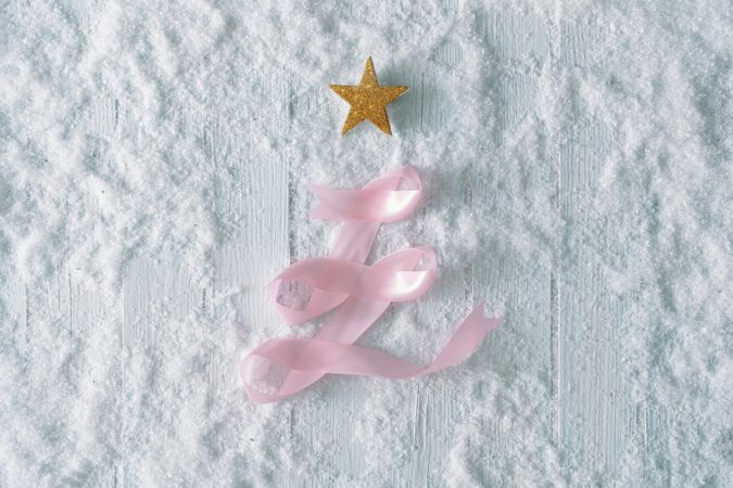 Wooden table background with snow and festive pink ribbon tree decoration