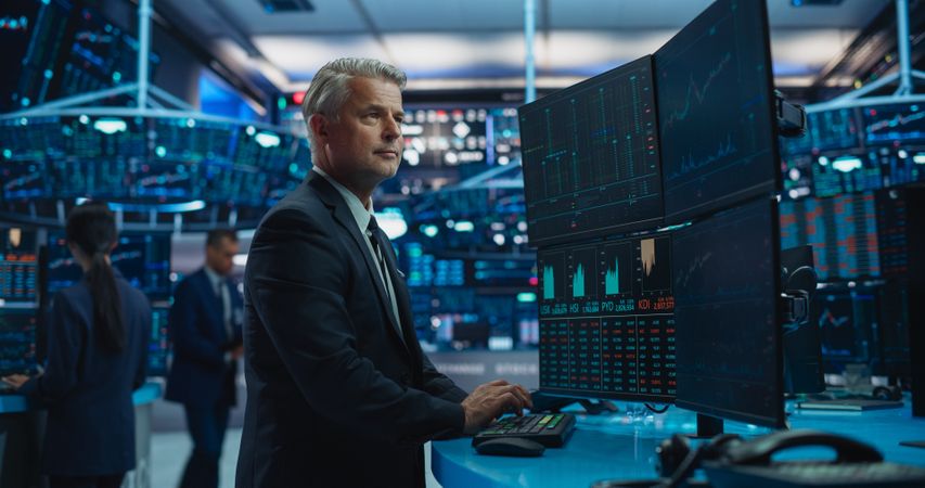 Financial Analyst Using a Desktop Computer with Multi-Monitor Workstation with Real-Time Graphs, Financial Reports and Market Charts.