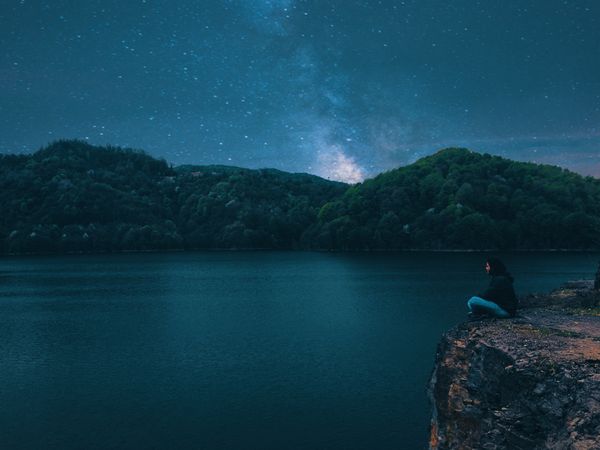 Side view of man sitting on rock near lake during night time