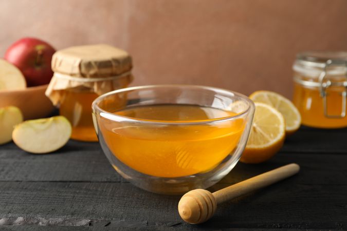 Bowl with honey, dipper and fruits on wooden background, space for text