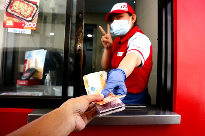 Fast food restaurant worker with facemask serving a customer at a drive thru facility