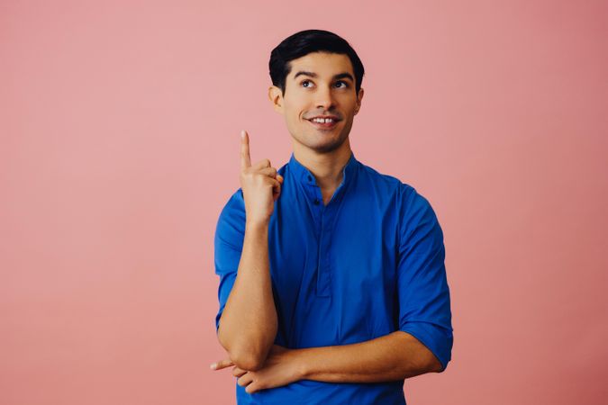 Medium shot of Latino man in pink studio looking up and pointing up