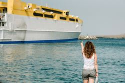 Curly woman looking at ship in water on seashore