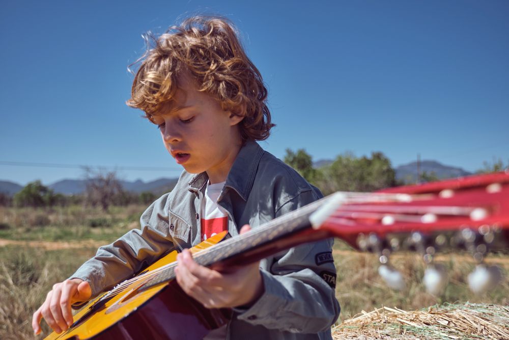 Little boy playing acoustic guitar on sunny day in countryside