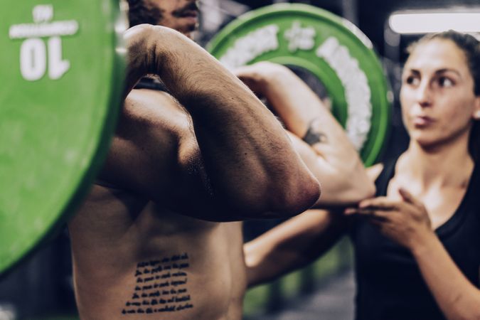 Muscular man lifting heavy weight in sport club and listening to personal trainer