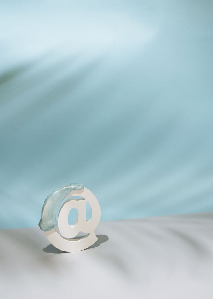Internet “at” symbol with palm leaf shadow in blue room, vertical