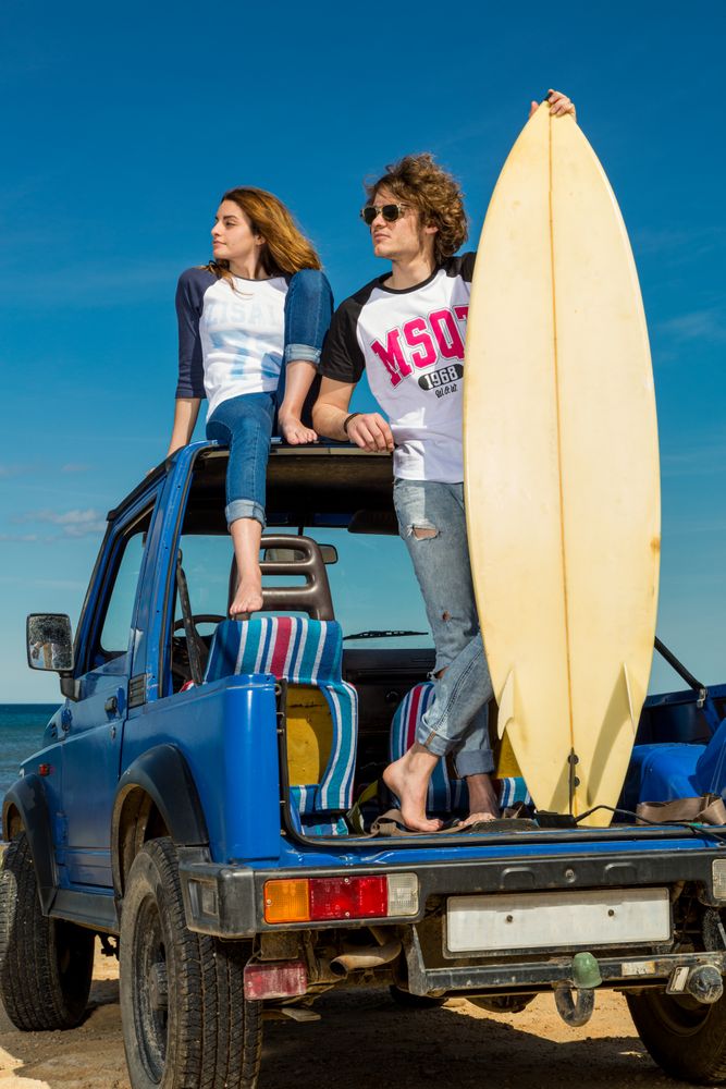 Guy with surfboard and woman on roof of car