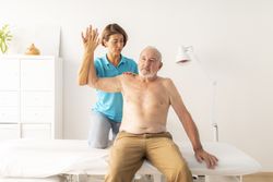 A female physiotherapist performs a massage and checks the mobility of the arm and shoulder of her mature patient