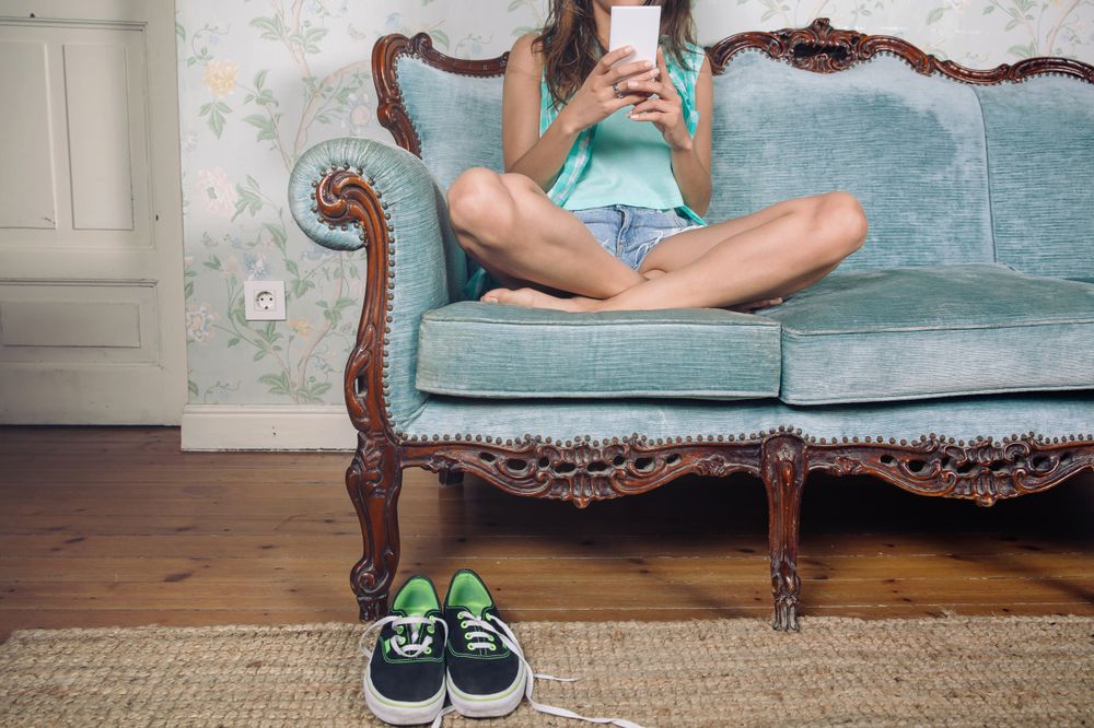 Woman sits crossed legged on sofa checking phone