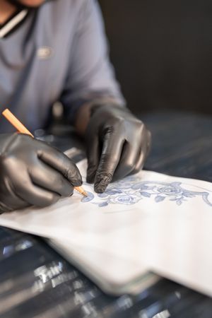 A tattoo artist is drawing a design stencil on his work stretcher before tattooing