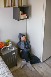 Depressed male teenager sitting on the floor in his bedroom