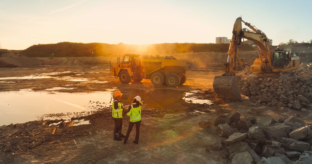 Aerial Drone Shot Of Construction Site On Sunny Evening: Industrial Excavators Digging Rocks And Loading Them Into Truck. Civil Engineer And Architect Observing Process, Discussing Real Estate Project