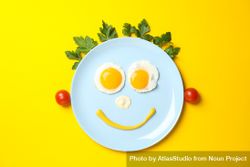 Looking down at blue plate with smiley face on it made of eggs and condiments, with vegetable hair 5RgqN4