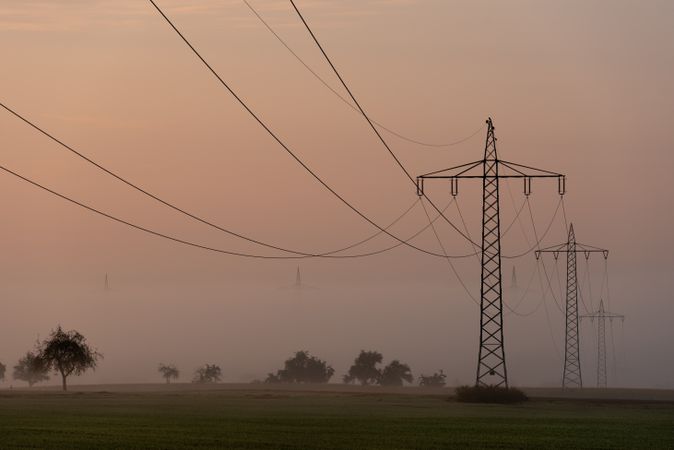 Electricity towers distribution through fog at sunrise, in a german village