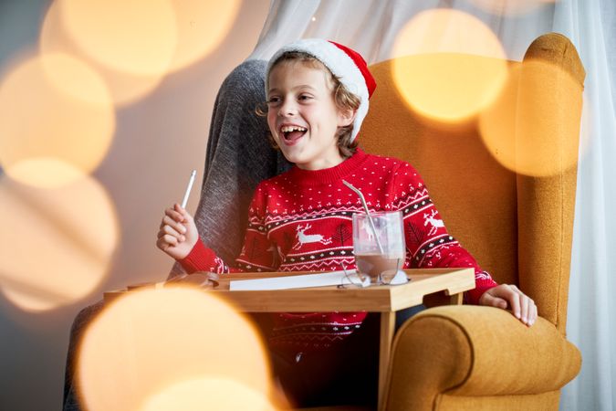 Happy boy in Santa hat writing letter on Christmas
