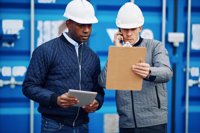 Two serious men in hard hats with a clipboard and tablet