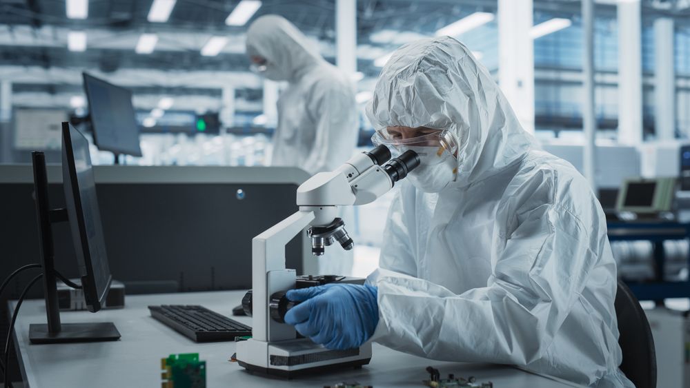 Person in hazmat protective suit looking through microscope