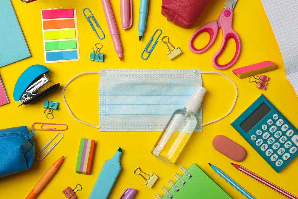 School supplies with medical mask and sanitizer on yellow background
