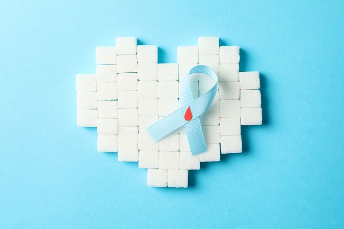 Diabetes awareness ribbon and heart made of sugar cubes on blue background