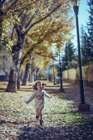 Happy child running in park of colorful fall leaves