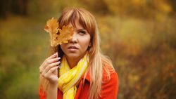 Female in red coat hiding half her face with fall leaf