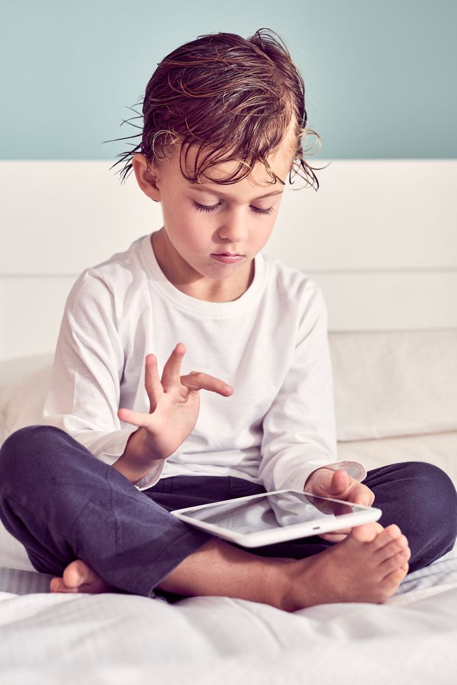 Serious boy playing game on tablet in bedroom