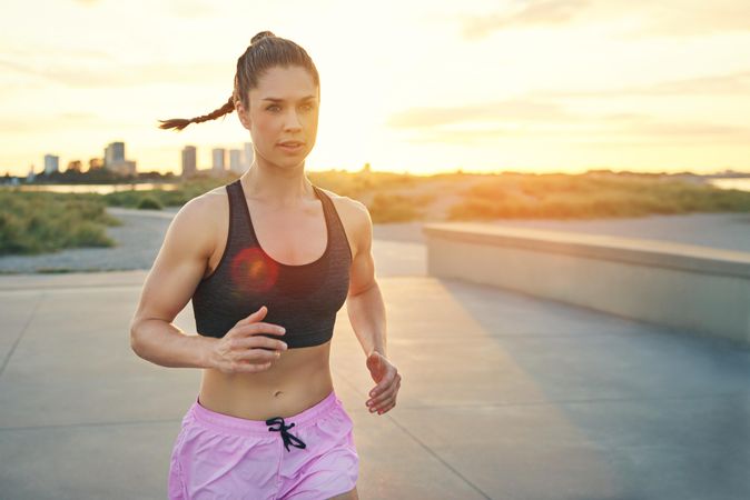 Woman running with cityscape in background at sunrise with sunflare