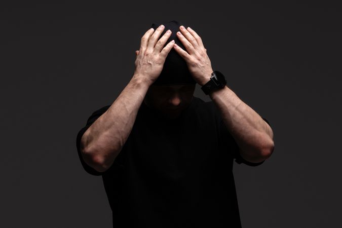 Man in beanie and sweatshirt holding head