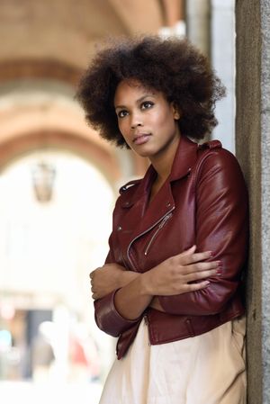 Woman standing in archway in red leather jacket and arms crossed