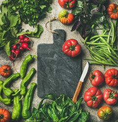 Fresh vegetables arranged with dark cutting board and knife in center, square crop