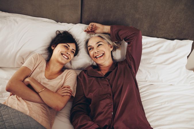 Smiling woman lying beside her mother on bed smiling with arms crossed