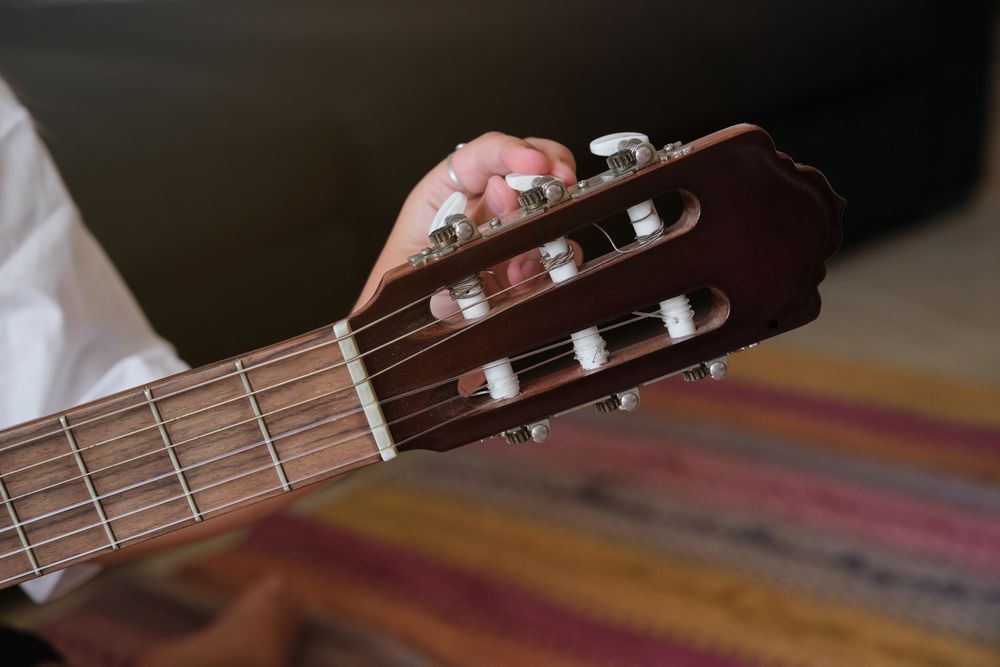 Crop person tuning acoustic guitar