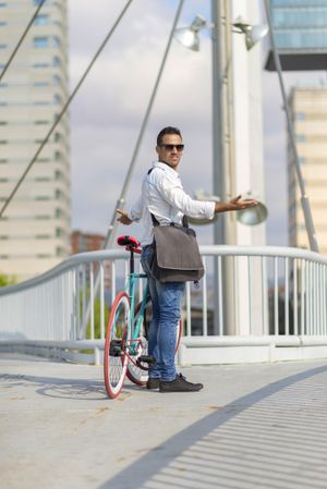 Confused male with bike between two paths on city bridge