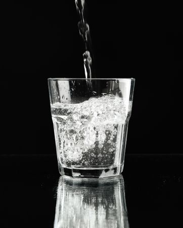 Dark room with single glass of water being poured