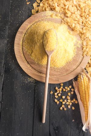 Pile of cornmeal on wooden plate with corn ears and kernels